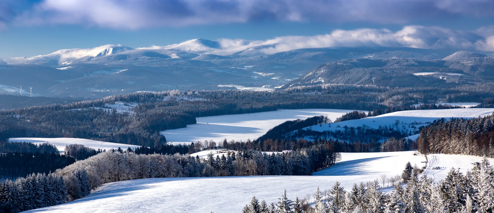 Winter panorama of the Broumovsko region – snowy meadows, forests and mountains beyond